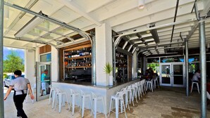 An outdoor bar area with a glass enclosure, white bar stools, and a variety of bottles on shelves. - Beach Haven 3 Bedroom Condo By Coastal Dreamin (Santa Rosa Beach)