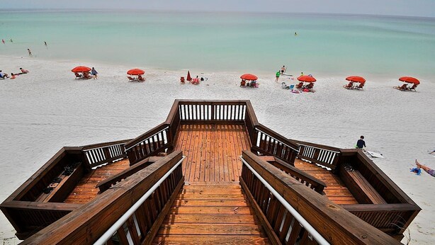 A wooden boardwalk leading to a beach with red umbrellas and lounge chairs. - Redfish Village M2 214 3 Bedroom Condo By Coastal Dreamin (Santa Rosa Beach)