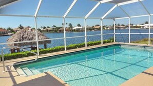 Zwembad met helder uitzicht op het water, een rieten constructie en een vergezicht op huizen en palmbomen.