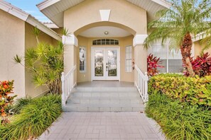 A building entrance with a covered walkway, a double door, and a small garden with various plants. - BE324 4 Bedroom Holiday Home by Marco Naples Vacation Homes (Marco Island)
