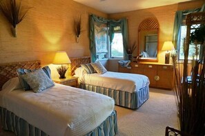Une chambre d’hôtel avec deux lits, un grand miroir, une fenêtre avec des rideaux et une tête de lit en bois.