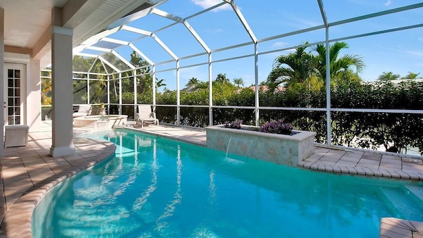 A swimming pool with a glass enclosure, surrounded by a patio area with chairs and a small table. - BRF335 3 Bedroom Holiday Home by Marco Naples Vacation Homes (Marco Island)