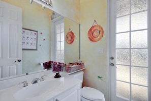 Un bagno con un lavandino bianco, uno specchio, un WC e una finestra con vetro smerigliato.