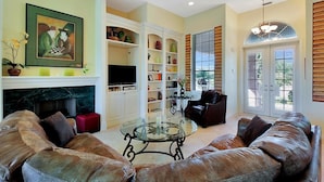 A living room with a leather sofa, a glass coffee table, a fireplace, a bookshelf, and a door with shutters. - BRF335 3 Bedroom Holiday Home by Marco Naples Vacation Homes (Marco Island)