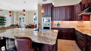 A spacious kitchen with dark wood cabinets, a granite countertop, and pendant lighting. - COPPER20 5 Bedroom Holiday Home by Marco Naples Vacation Homes (Marco Island)