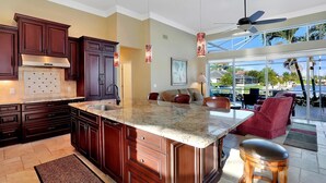 A spacious kitchen with dark wood cabinets, a large island with a granite countertop, and a ceiling fan. - COPPER20 5 Bedroom Holiday Home by Marco Naples Vacation Homes (Marco Island)