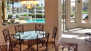 Un comedor con mesa de vidrio y sillas de metal, con vista a una piscina y zona de estar al aire libre.