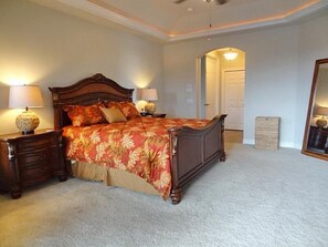 Ein Schlafzimmer mit einem großen Bett, zwei Nachttischen, einem Spiegel und einer Tür zu einem weiteren Raum.