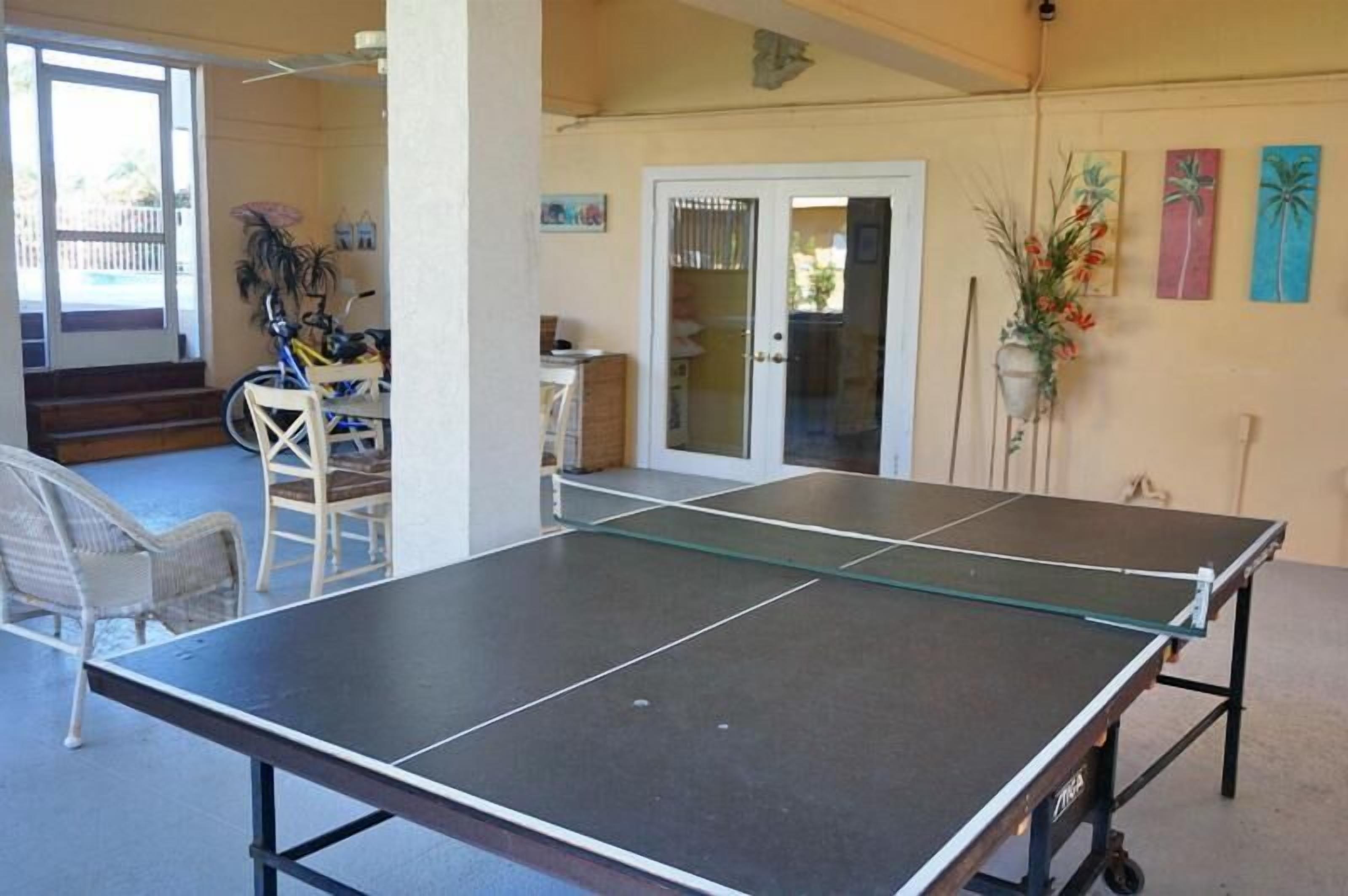 A room with a ping pong table, a chair, and a door leading outside.