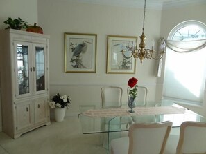 Un coin repas avec une table en verre, des chaises blanches, un lustre et des œuvres d’art encadrées accrochées au mur.