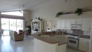 A spacious kitchen with white cabinets, a central island, and a dining area with a sofa and chairs. - KEN486 3 Bedroom Holiday Home by Marco Naples Vacation Homes (Marco Island)