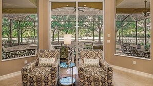 A room with a large window, two patterned armchairs with 'BEACH HOUSE' pillows, a small round table, and a ceiling fan. - MAJ8978 4 Bedroom Holiday Home by Marco Naples Vacation Homes (Naples)