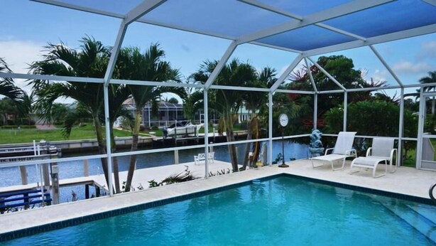 A swimming pool with a covered area, white lounge chairs, and a view of the surrounding landscape.