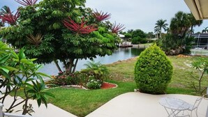 A patio area with a view of a lake, surrounded by lush greenery and a small table with chairs.