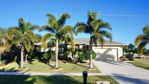 A residential house with a front yard, palm trees, and a driveway.