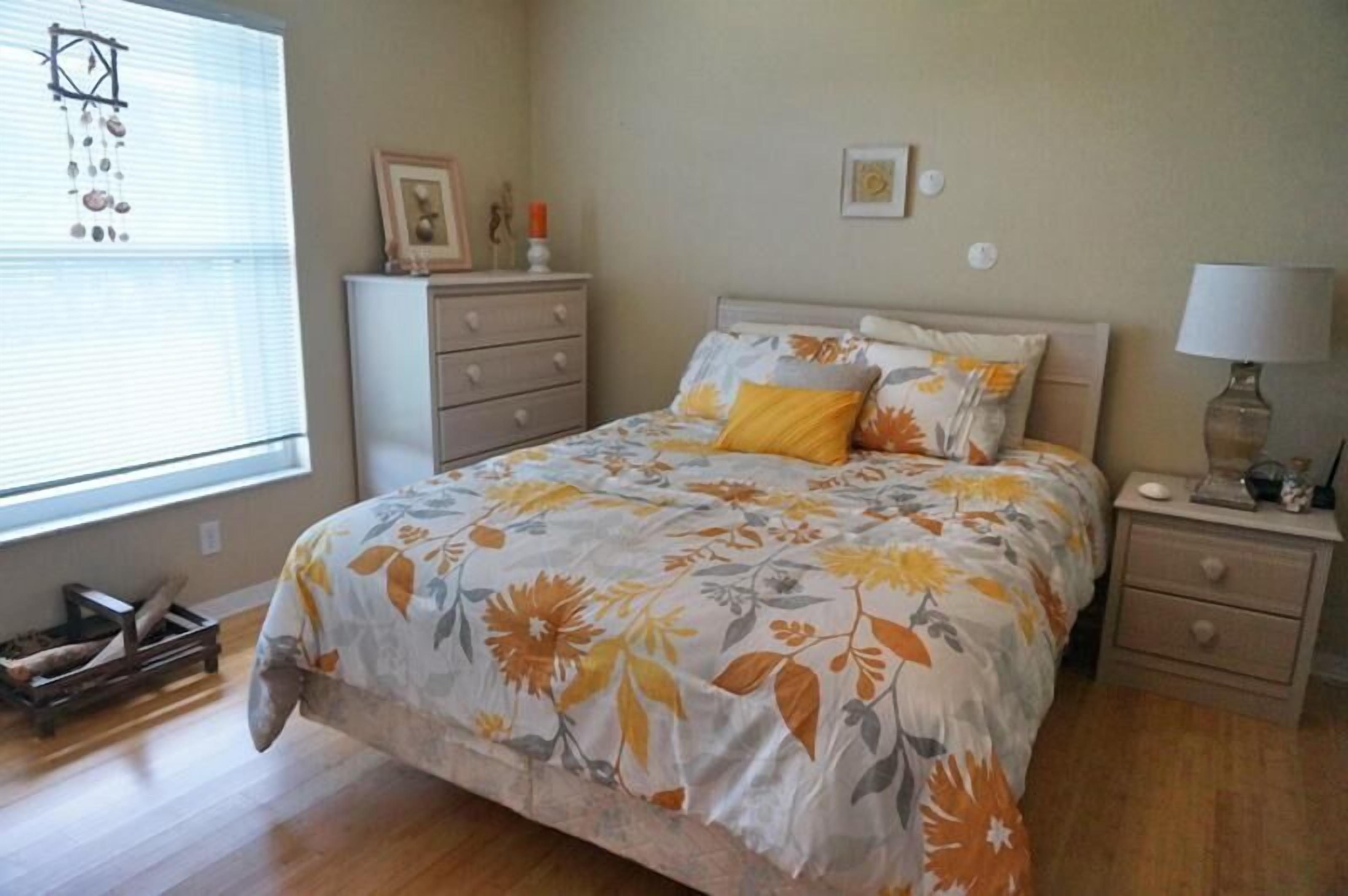 A bedroom with a bed, a nightstand, a dresser, and a window with blinds.