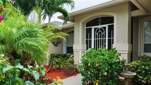 A house with a well-maintained garden, a stone fountain, and a large window with decorative bars.