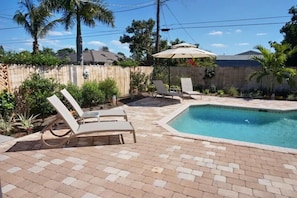 A backyard with a swimming pool, two lounge chairs, and an umbrella.
