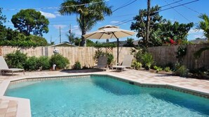 A backyard with a swimming pool, a wooden fence, and a patio area with chairs and an umbrella.