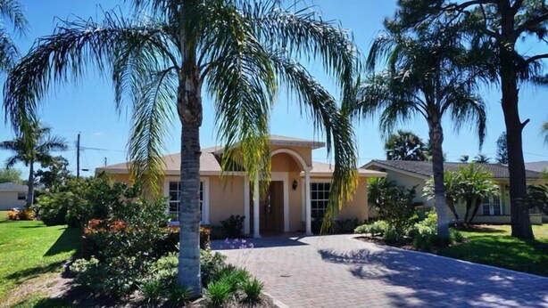 A two-story house with a central entrance, surrounded by a well-maintained lawn and palm trees.