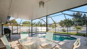 A covered outdoor patio with a glass table, chairs, and a pool.