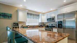A modern kitchen with white cabinets, a granite countertop, stainless steel appliances, and a bar area with stools.