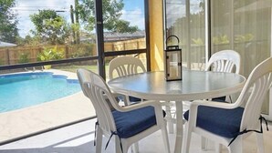 A glass-top table with white chairs and blue cushions, overlooking a swimming pool. - NP97TH 730 3 Bedroom Holiday Home by Marco Naples Vacation Homes (Naples)