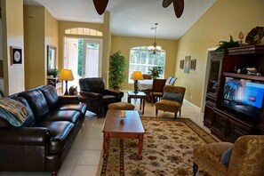 A living room with a dark brown leather sofa, a wooden coffee table, and a television on a wooden stand. There is a patterned rug on the floor, and a window with blinds in the background. - SHEF2024 4 Bedroom Holiday Home by Marco Naples Vacation Homes (Marco Island)
