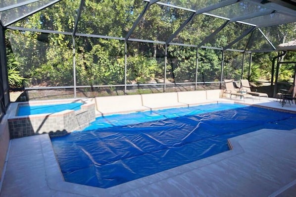 An indoor swimming pool with a glass enclosure, surrounded by lounge chairs and a covered patio area.