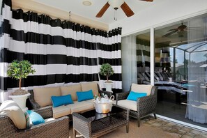 A sunlit patio area with a black and white striped curtain backdrop, wicker furniture, and potted plants. - SMARCO1601 4 Bedroom Holiday Home by Marco Naples Vacation Homes (Marco Island)