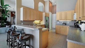 A modern kitchen with a central island, bar stools, wooden cabinets, and a refrigerator.