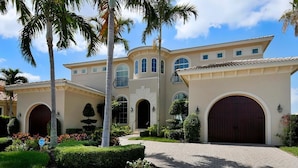 A large, two-story house with a driveway, palm trees, and a well-maintained garden.