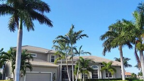 A two-story house with a garage, surrounded by palm trees and a well-maintained lawn.