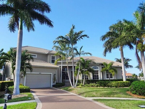 A two-story house with a garage, surrounded by palm trees and a well-maintained lawn.