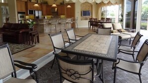 A spacious living area with a large dining table, comfortable seating, a kitchen area, and a view through large windows.