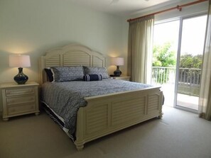 A bedroom with a large bed, two bedside tables, and a view of a balcony.