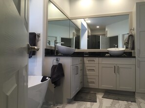 Un baño moderno con un espejo grande, dos lavamanos, una bañera y un perchero para toallas.