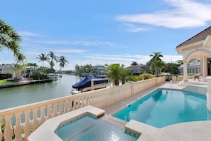 A swimming pool with a view of a canal and palm trees, a covered boat dock, and a building with a tiled roof. - SPIN509 4 Bedroom Holiday Home by Marco Naples Vacation Homes (Marco Island)