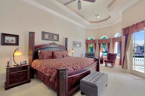 A spacious bedroom with a large bed, a sitting area with a chair, and a view of the outdoors through large windows. - SPIN509 4 Bedroom Holiday Home by Marco Naples Vacation Homes (Marco Island)