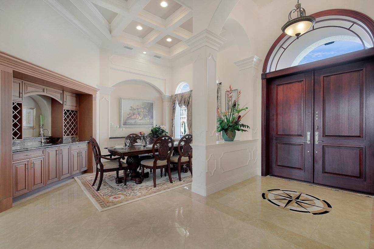 A spacious dining area with a large wooden table and chairs, a kitchen with pink cabinets, and a dark wooden double door.