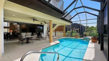 An indoor swimming pool with a glass ceiling, surrounded by lounge chairs and a dining area.