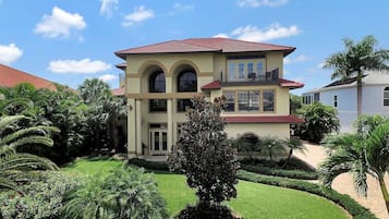 A two-story house with a red-tiled roof, a balcony on the upper floor, and a well-maintained garden with various plants and a lawn.