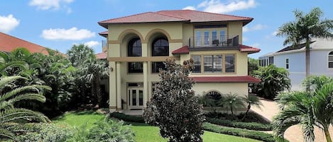 A two-story house with a red-tiled roof, a balcony on the upper floor, and a well-maintained garden with various plants and a lawn.