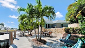 A wooden dock leading to a patio area with a table and chairs, surrounded by palm trees and a stone wall. - WH1074 3 Bedroom Holiday Home by Marco Naples Vacation Homes (Marco Island)