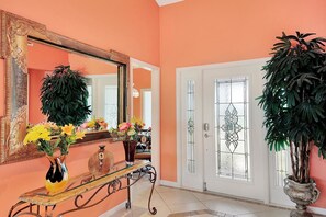 A hallway with a large mirror, a glass door with a decorative glass panel, and two potted plants. - WH1074 3 Bedroom Holiday Home by Marco Naples Vacation Homes (Marco Island)