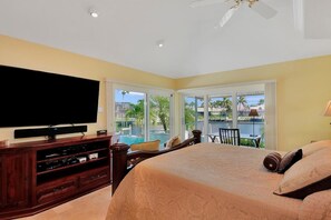 A bedroom with a large bed, a TV, and a view of a pool and palm trees. - WH1074 3 Bedroom Holiday Home by Marco Naples Vacation Homes (Marco Island)