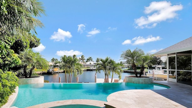 A swimming pool with a curved design, surrounded by palm trees and a clear sky. - WH1074 3 Bedroom Holiday Home by Marco Naples Vacation Homes (Marco Island)