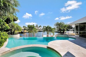 A swimming pool with a curved design, surrounded by palm trees and a clear sky. - WH1074 3 Bedroom Holiday Home by Marco Naples Vacation Homes (Marco Island)