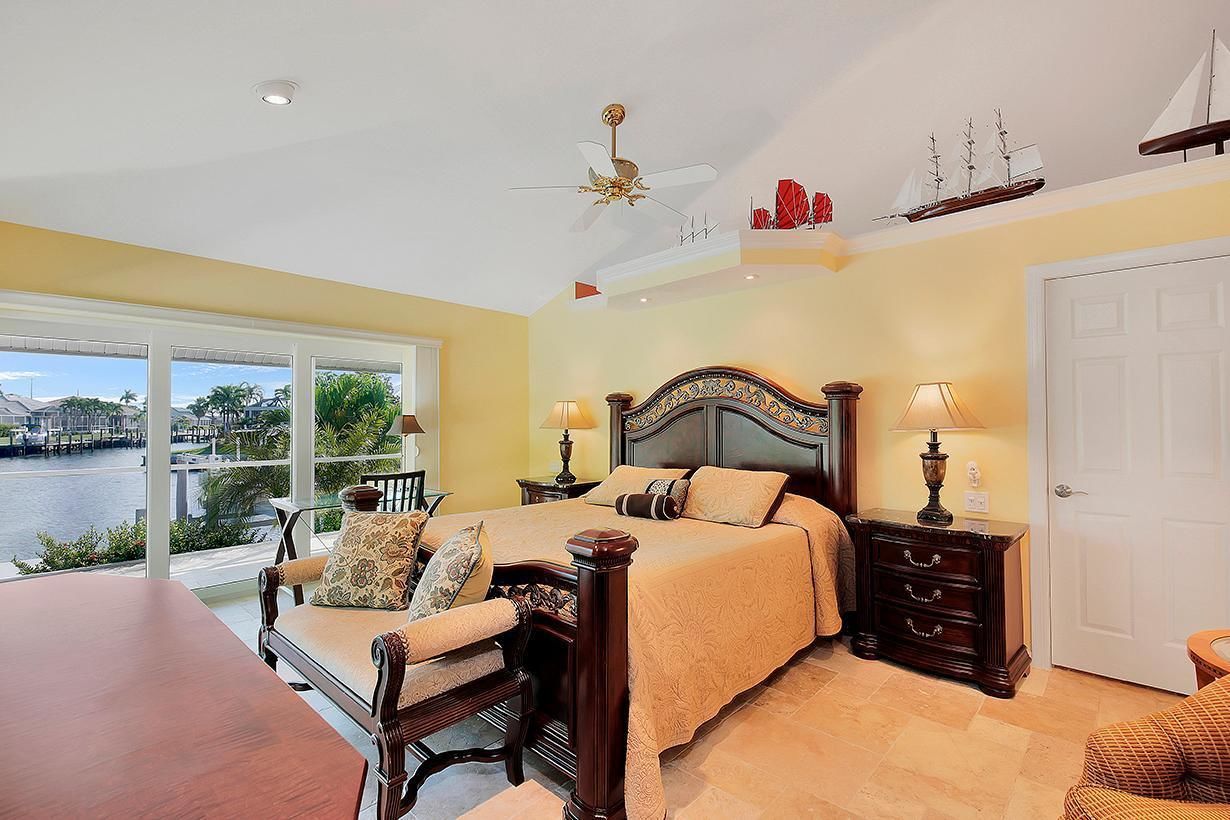 A bedroom with a large bed, two bedside tables, a chair, a desk, and a view of a marina.