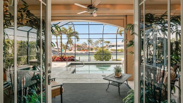 Un espace piscine intérieur moderne, doté d’une paroi vitrée, d’un ventilateur de plafond et d’une table avec des chaises.